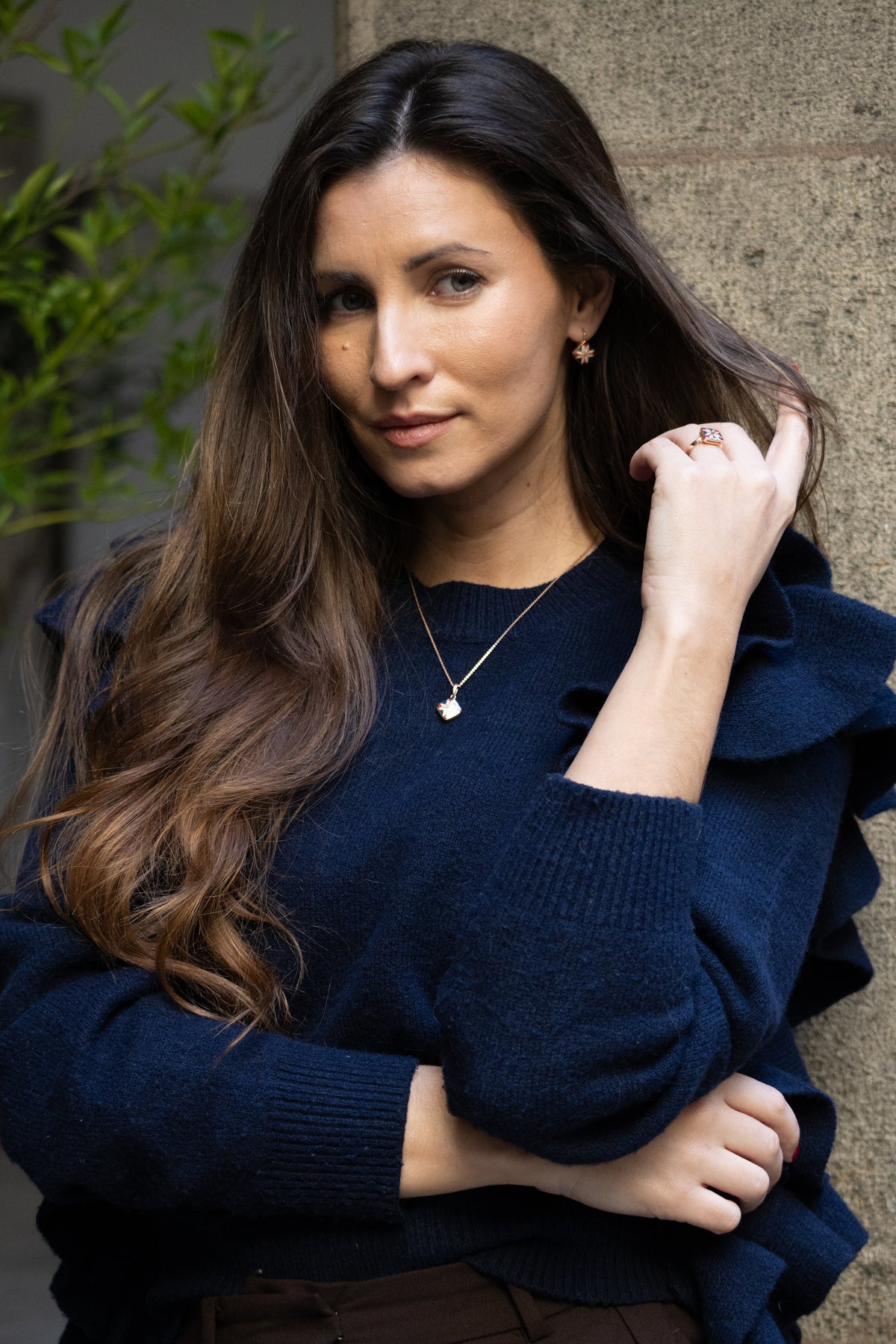 Woman wearing a navy blue sweater with ruffled shoulders against a stone wall.