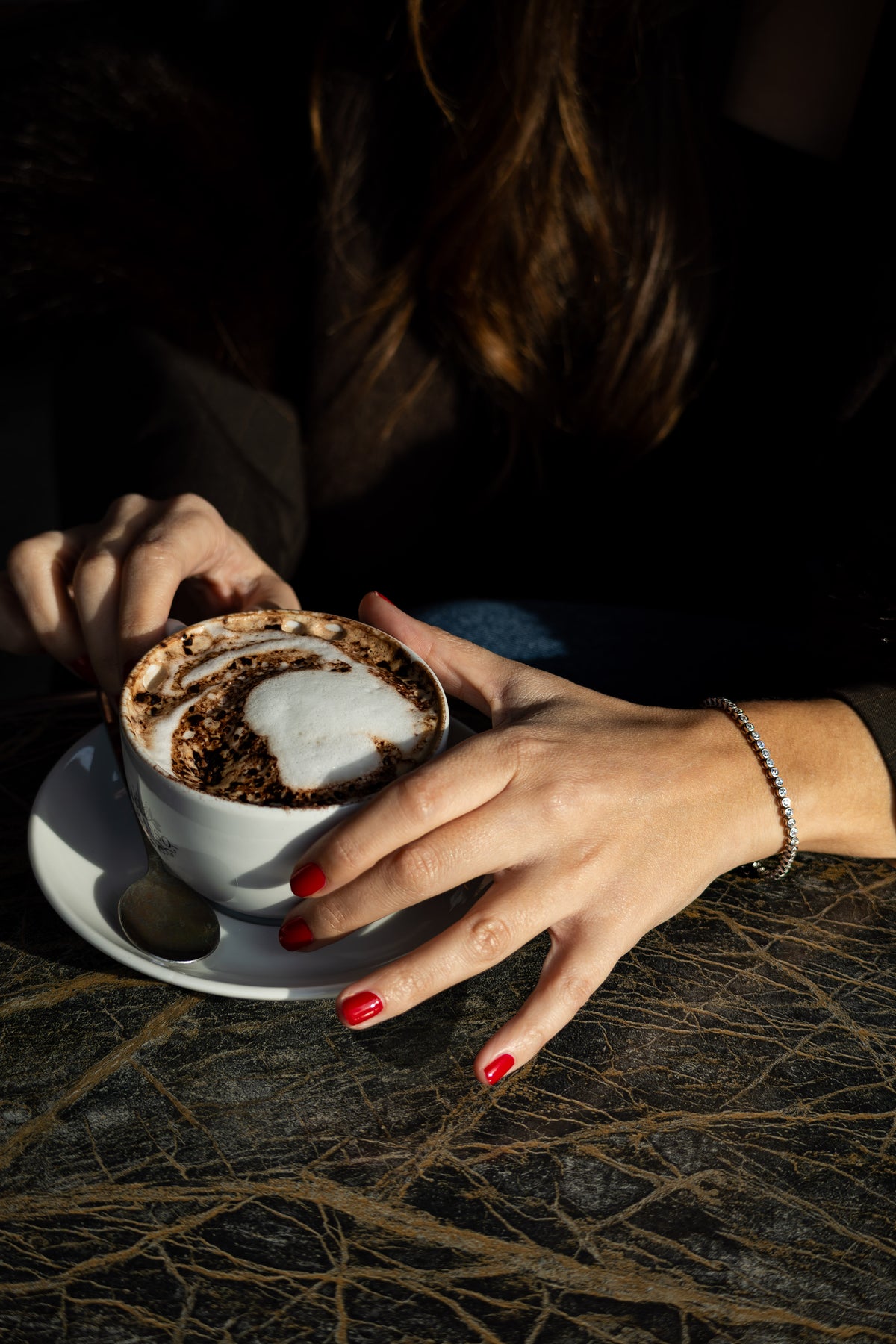 Person holding a cup of cappuccino with a dark background silver braclet