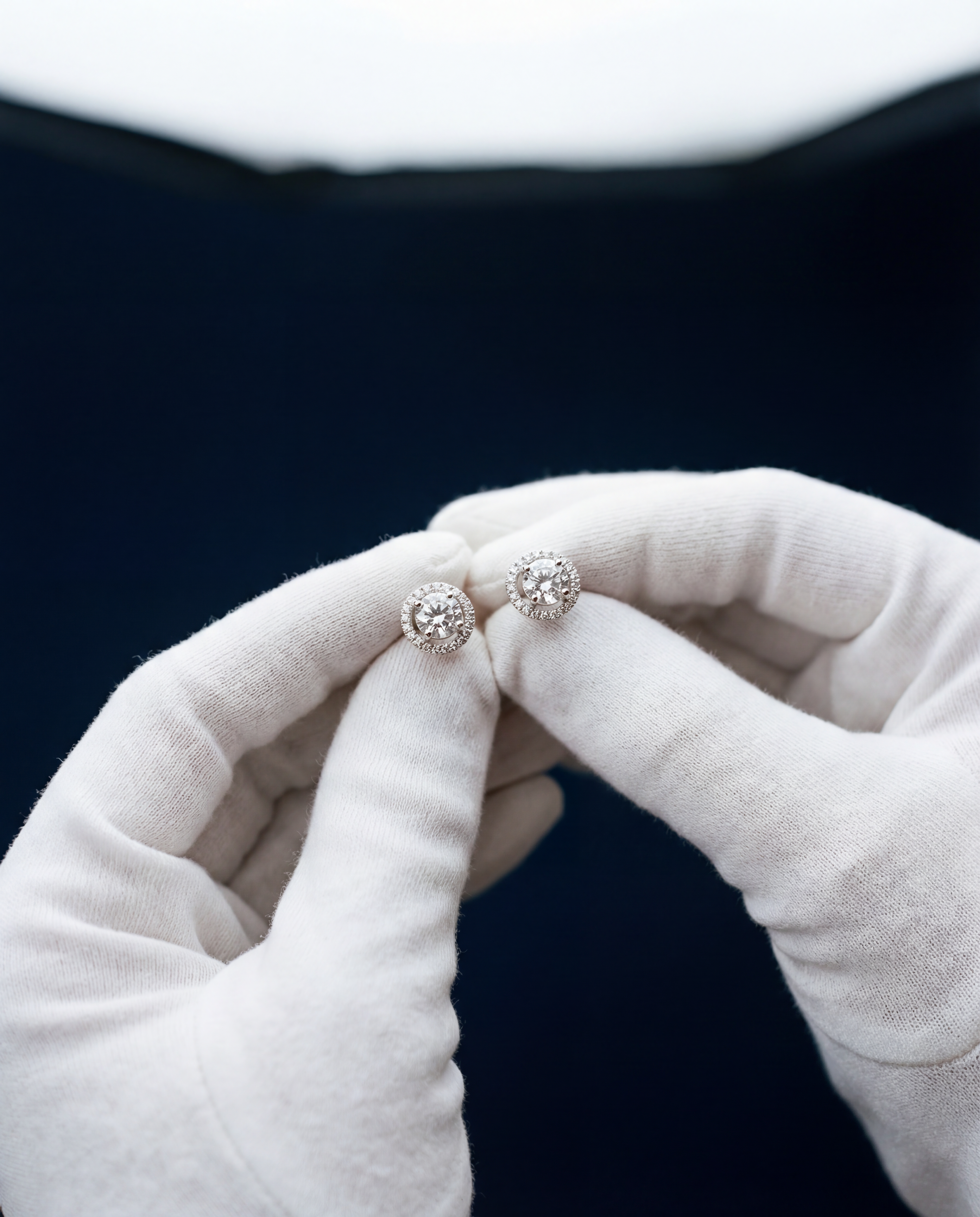 Pair of diamond earrings held by a gloved hand 